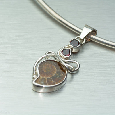 Small ammonite silver pendant with two feature garnet gemstones.